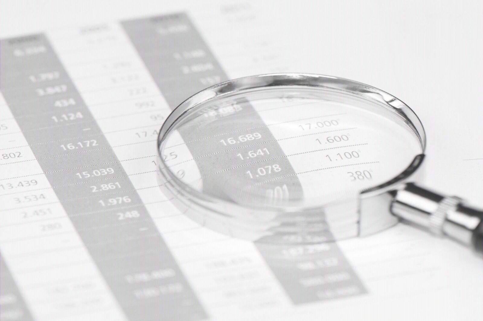 Ein Vergrößerungsglas, das über eine Finanztabelle gehalten wird und die Zahlen und Ziffern in den schwarz-grau gedruckten Zeilen und Spalten vergrößert.