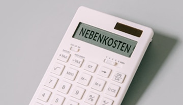 Ein weißer Taschenrechner zeigt auf seinem Bildschirm das Wort NEBENKOSTEN an, was so viel wie Nebenkosten bedeutet. Der Rechner steht auf einer hellgrauen Fläche.